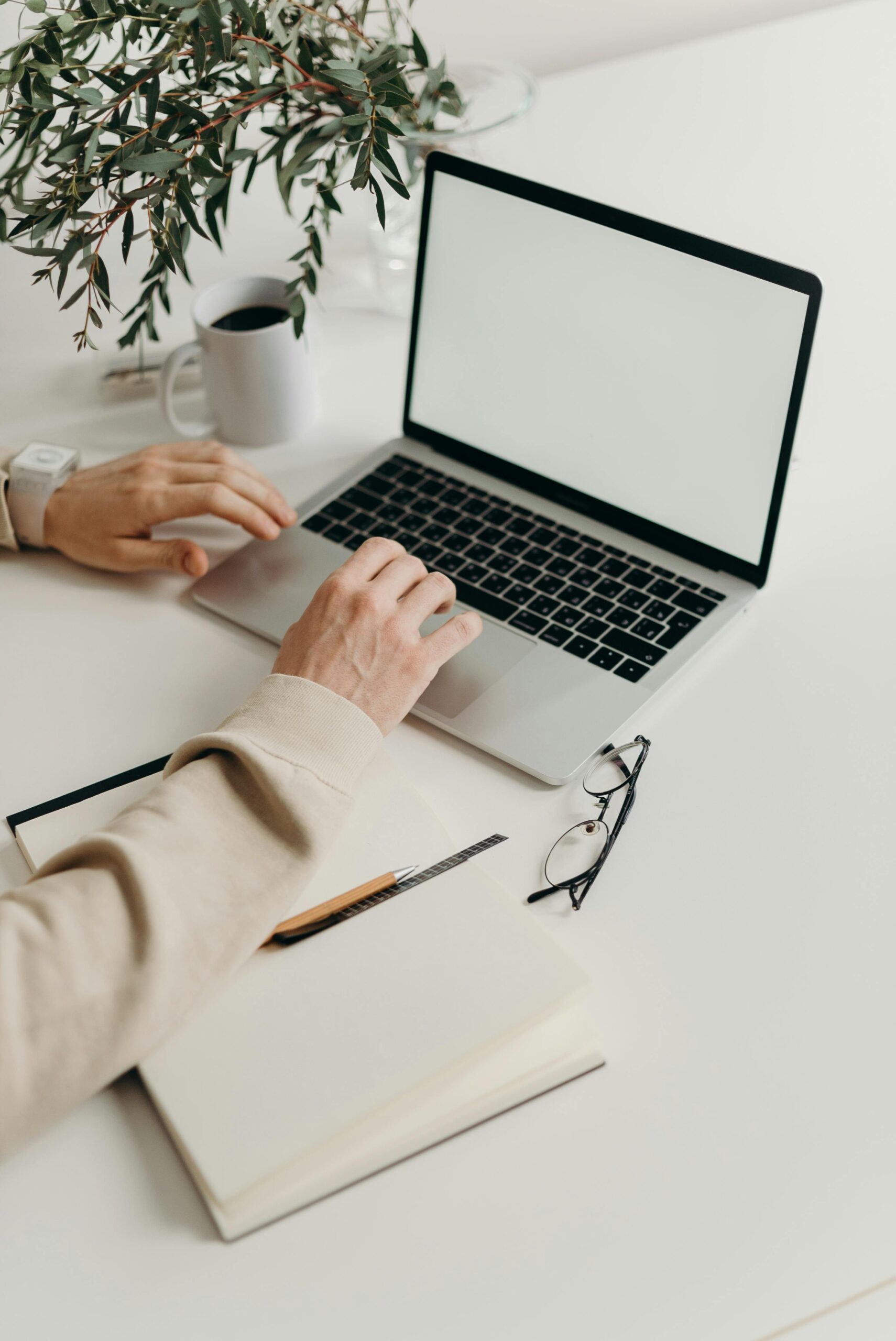 A close up of someone using a laptop with glasses and a notebook nearby